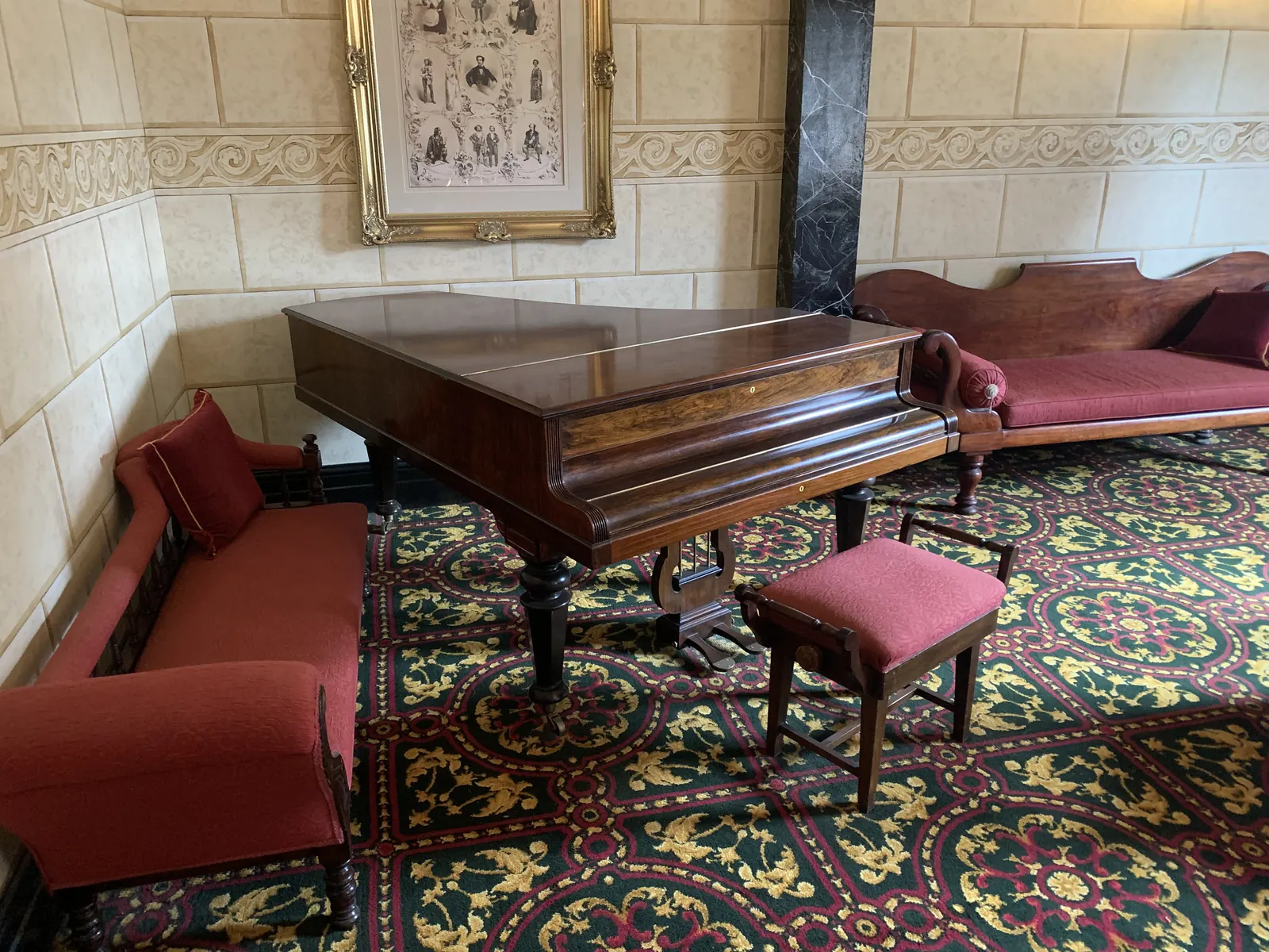 Victorian parlour with a piano, red chairs and patterned carpet